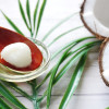 Cuchara de palo con aceite de coco al lado de un coco partido a la mitad.