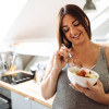 Mujer embarazada comiendo de un bowl en una cocina.