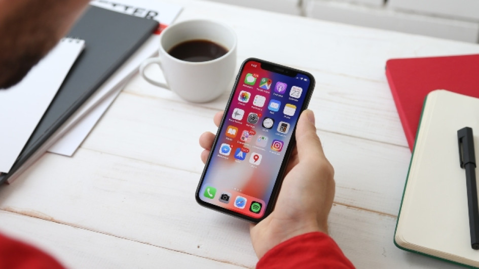 Mejores-apps-para-ayuno-intermitente Hombre mirando su iPhone en un escritorio al lado de un cuaderno y un café.