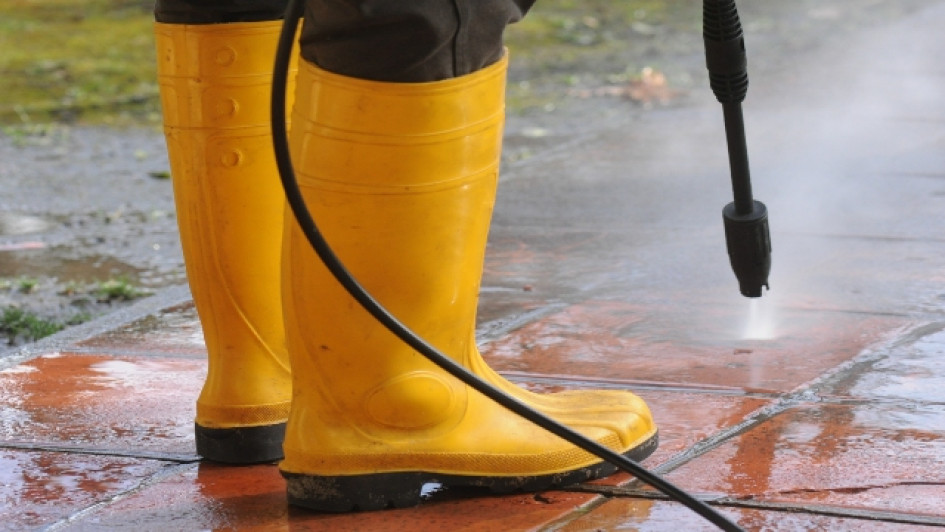 Mejores-hidrolavadoras-del-mercado Persona con botas de goma amarillas usando una hidrolavadora en el piso.