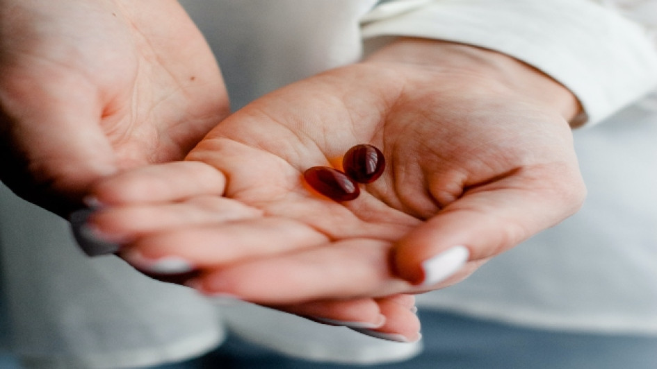 Complejo-b-para-que-sirve Manos de una mujer con dps cápsulas de vitaminas rojas.