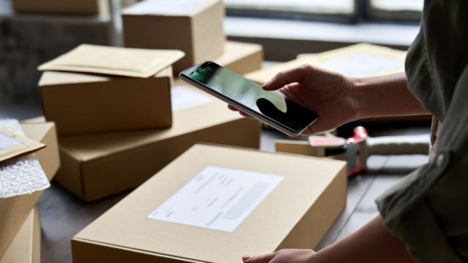 Como-vender-en-Amazon-desde-Colombia Persona con un celular escanea un código de barras en una caja de cartón.