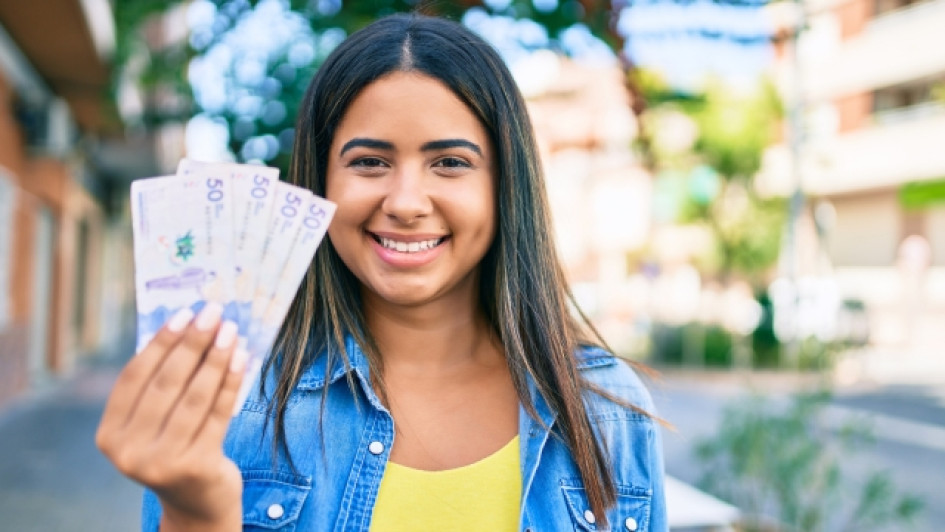 Jovenes-en-Accion-como-consultar-con-cedula-si-es-beneficiario Mujer sonriendo mostrando billetes de Colombia en su mano derecha.