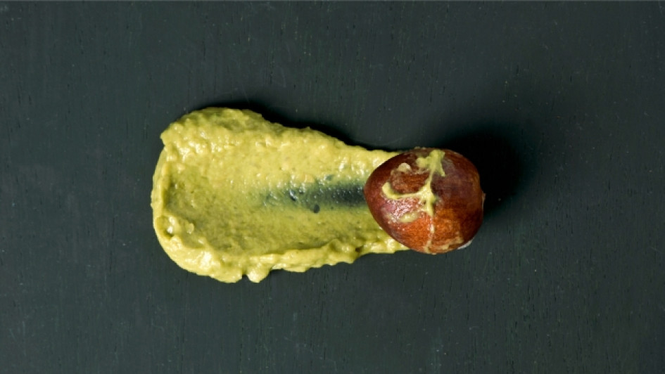 Para-qué-sirve-el-agua-de-la-pepa-de-aguacate Pepa de aguacate cubierta en parte por guacamole en una superficie negra.