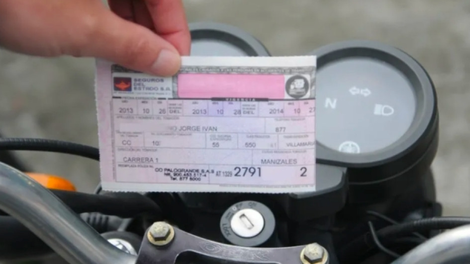 Como-saber-si-mi-soat-esta-vigente Persona sosteniendo un SOAT frente al tablero de una moto.