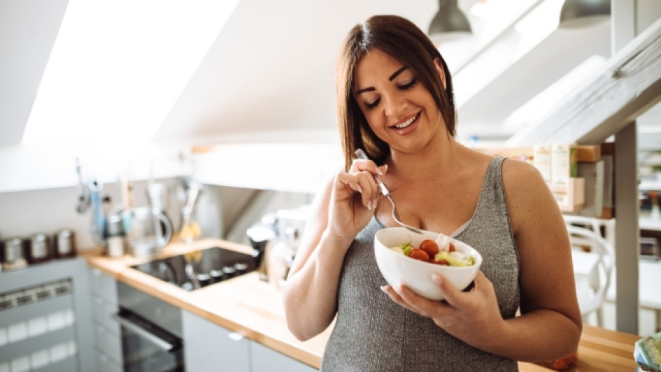 Una-mujer-embarazada-puede-comer-picante Mujer embarazada comiendo de un bowl en una cocina.