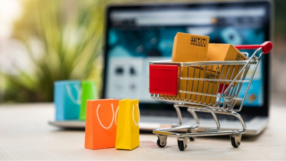 Mejores-promociones-Black-Friday-Colombia Carrito de compras con bolsas adentro con un computador portatil detrás