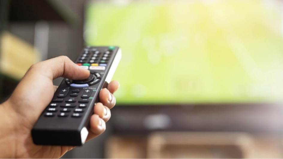 Mejor-cojin-para-ver-tv Mano sosteniendo un control de TV con el TV de fondo