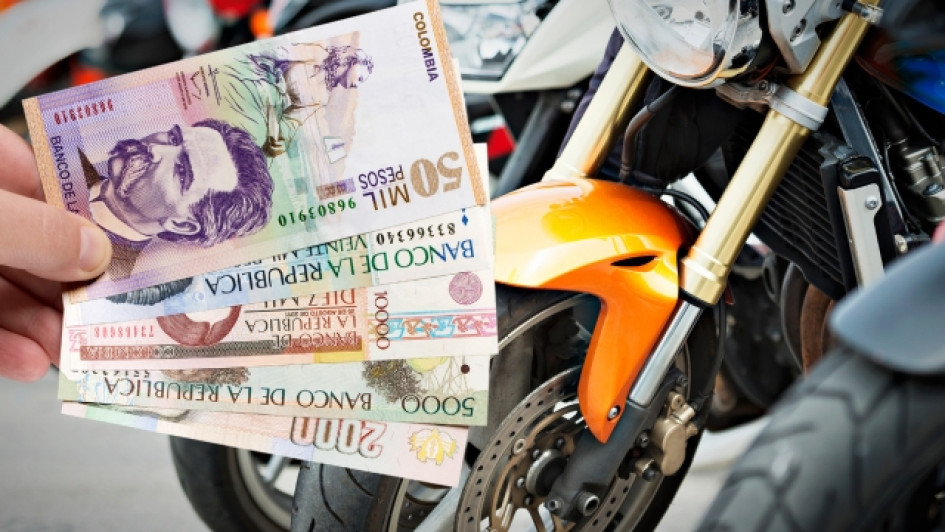 Consultar-impuestos-de-moto-por-placa Mano sosteniendo billetes de pesos colombianos frente a varias motos.
