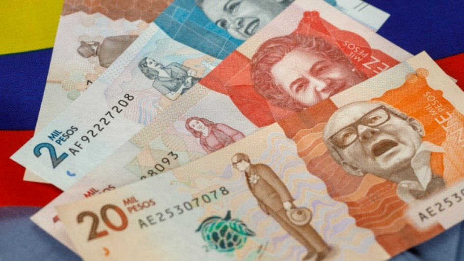 Aportes-parafiscales-que-son-quien-los-paga-como-se-liquidan Billetes de pesos colombianos con una bandera de Colombia detrás.
