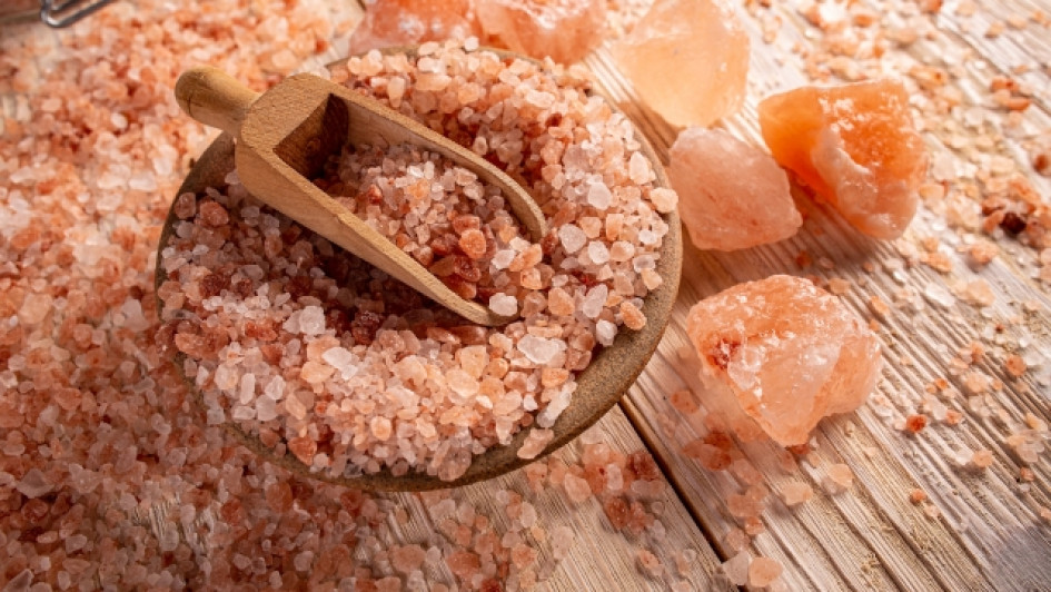 Para-que-sirve-la-sal-rosa-de-himalaya Mesa con sal rosa del Himalaya, un plato y una cuchara de madera.