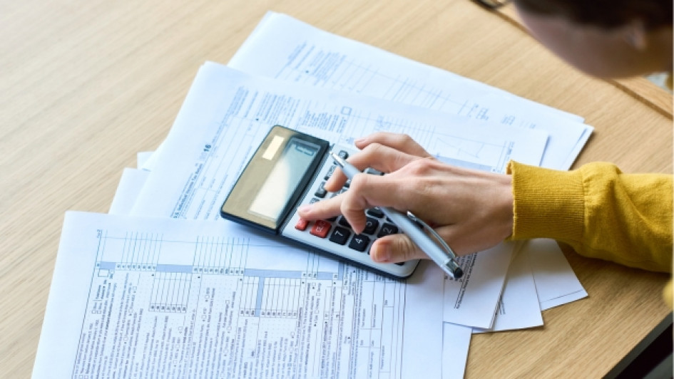 Impuesto-predial-que-es-como-pagarlo Mano usando una calculadora encima de unos papeles