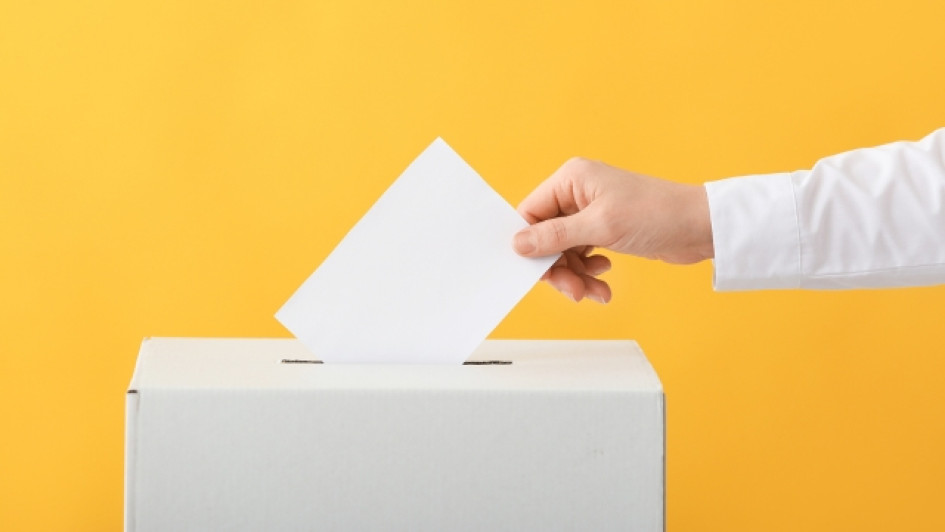 Cuantos-votos-se-necesitan-para-ser-diputado-en-colombia Meno introduciendo un voto en una caja. Fondo amarillo.