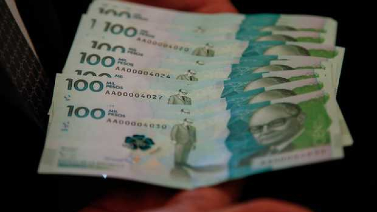 Dos manos sosteniendo billetes de 100 mil pesos Colombianos